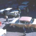 Patti Dykes maneuvers her 1957 Ford Fairlane out of the parking lot past the white 1959 Chevy Impala (to her right) and blue and white 1956 Buick (to her left). Parked in the shadows in the back are a '55 Chevy, 1954 Studebaker and 1956 Dodge. This photo was taken out the study hall window on the second floor, looking down on the space soon to be filled with the new administrative office complex. The students are leaving school on a September 1959 Friday afternoon. Patti's Fairlane was considered a very stylish car because it was one of the first "hardtop coupes," so named because there were no side pillars between the front and rear windows. This was supposed to give it the appearance of a convertible while retaining the warmth and comfort of a hard top. Notice on the rear bumper the license plate bracket is offset to the right, another sporty option. Ferguson students of the 59-60 school year debated constantly whether Patty's Ford, the white Chevy Impala, Haskell Sullivan's Chevy, or the 1951 Shoebox Ford was the hottest car in town.